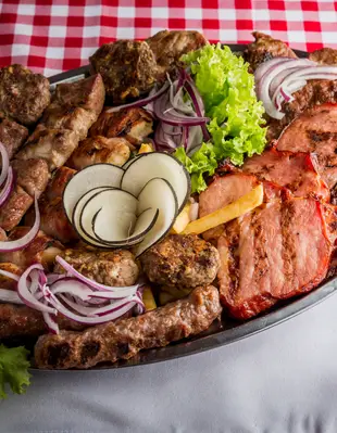 Raznovrsno meso na ovalnom tanjiru sa povrćem.