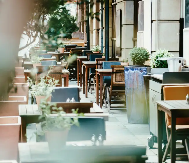Prazna terasa restorana sa stolovima i cvećem.